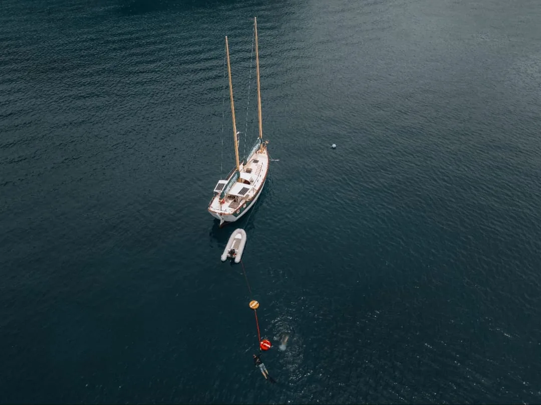 Aerial view of SV Freedom Fargo at anchor with her dinghy, buoy line and a freediver at the surface