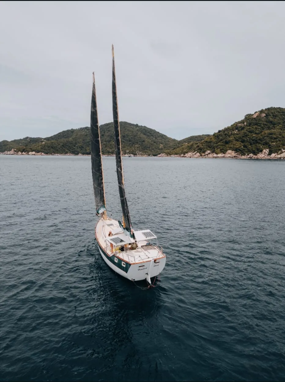 SV Freedom Fargo under sail in front of the green hills of Koh Tao