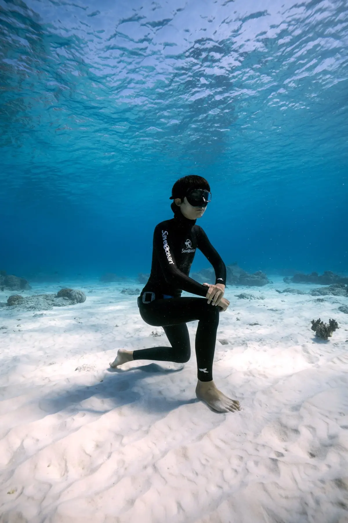 Freediver resting on one knee on the white sandy bottom in the shallows off Koh Tao