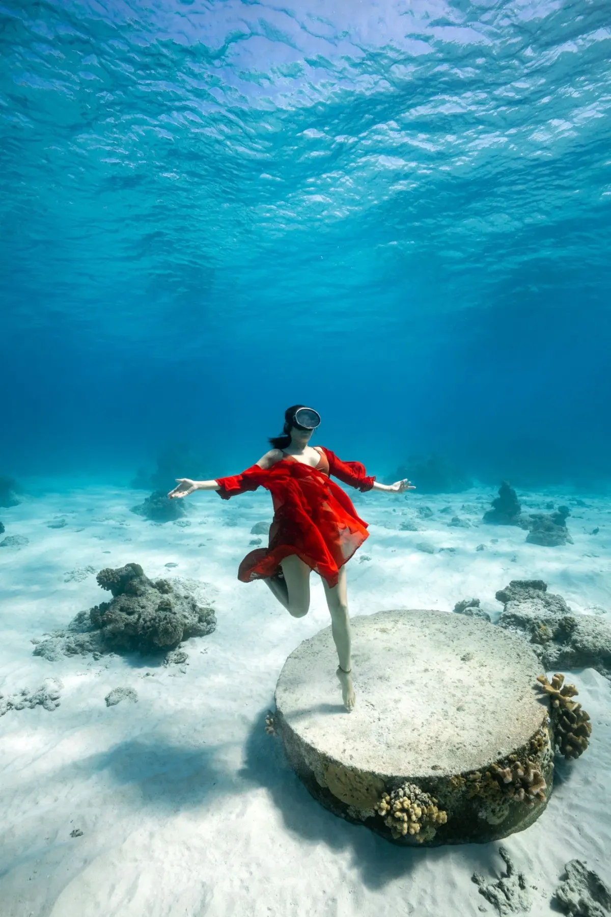 Underwater photoshoot off Koh Tao, a model in a flowing red dress posing on the sandy bottom