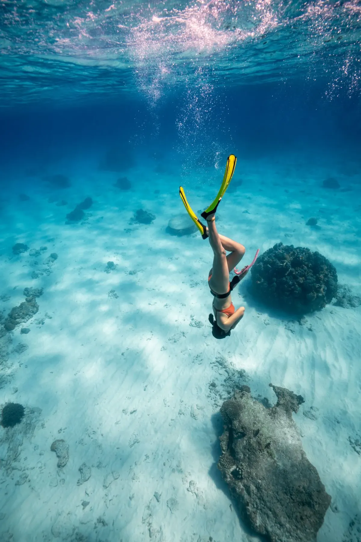 Snorkeler duck diving with yellow fins over the turquoise sand flats of Koh Tao