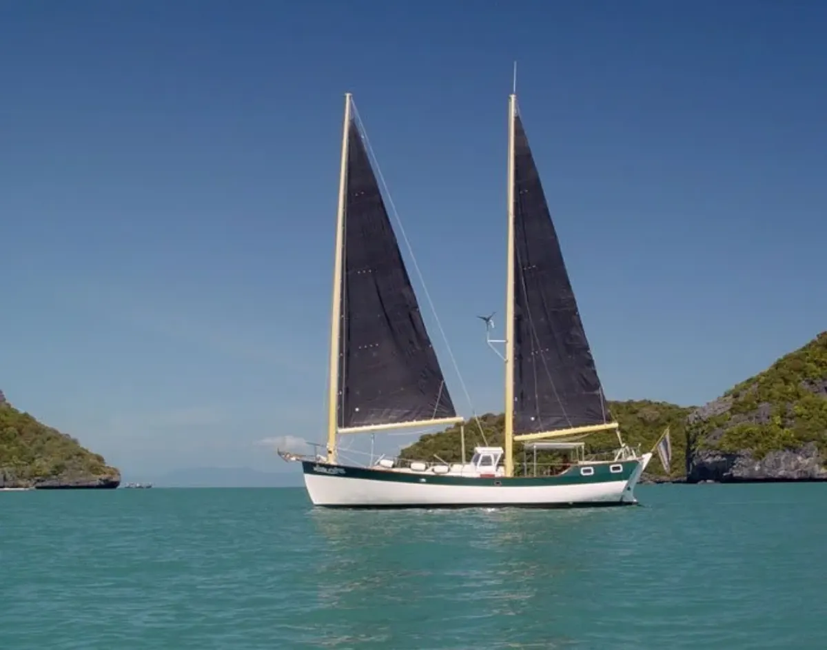 SV Freedom Fargo at anchor with her dark sails up between the green islands of the Gulf of Thailand