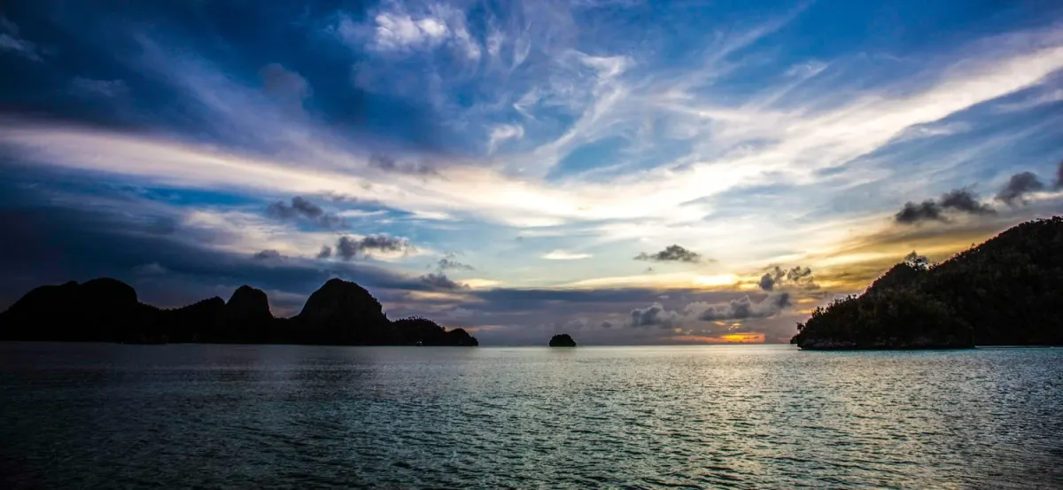 Sunset over the Gulf of Thailand, island silhouettes and open sky seen from the boat